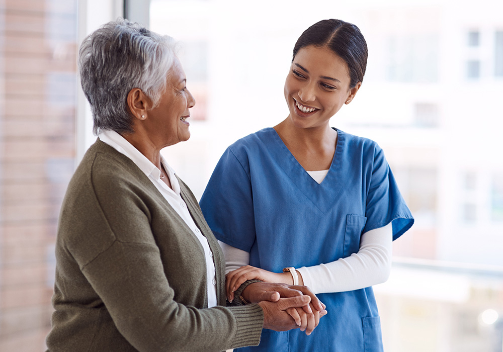 A caregiver with an elderly woman steadying herself on the caregivers arm